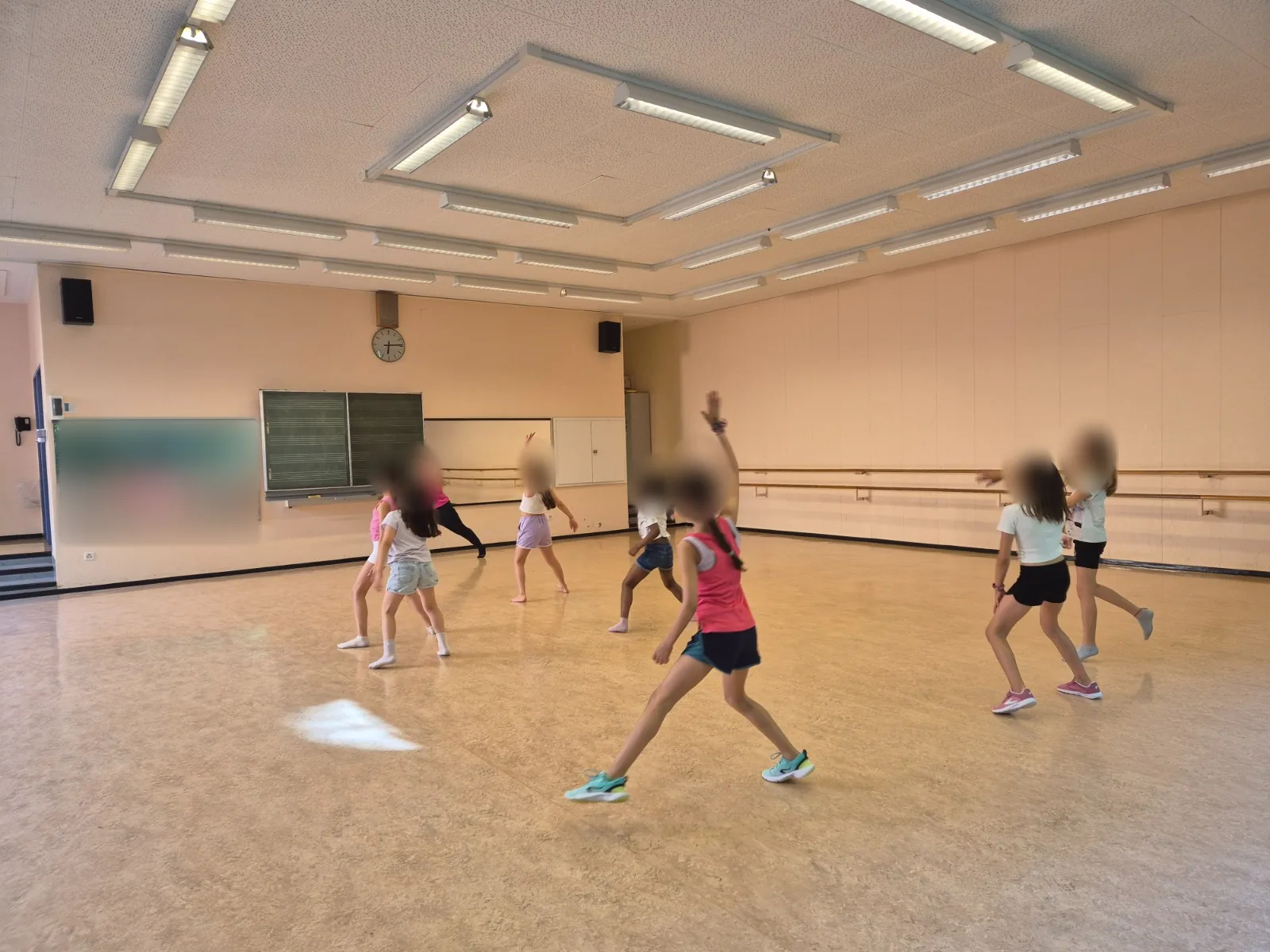 Des enfants suivent un cours de danse dans une salle, avec leurs visages anonymisés